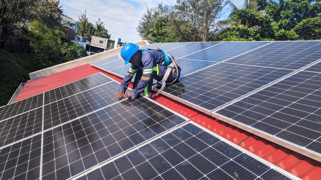 Technicien Alona Energy avec casque bleu et harnais de sécurité complet fixant des panneaux en toiture rouge