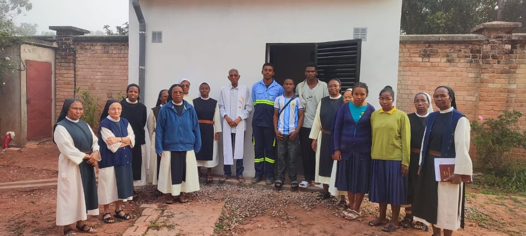 Remise officielle du projet — religieuses, prêtre et techniciens Alona Energy devant la salle technique du couvent de Fianarantsoa