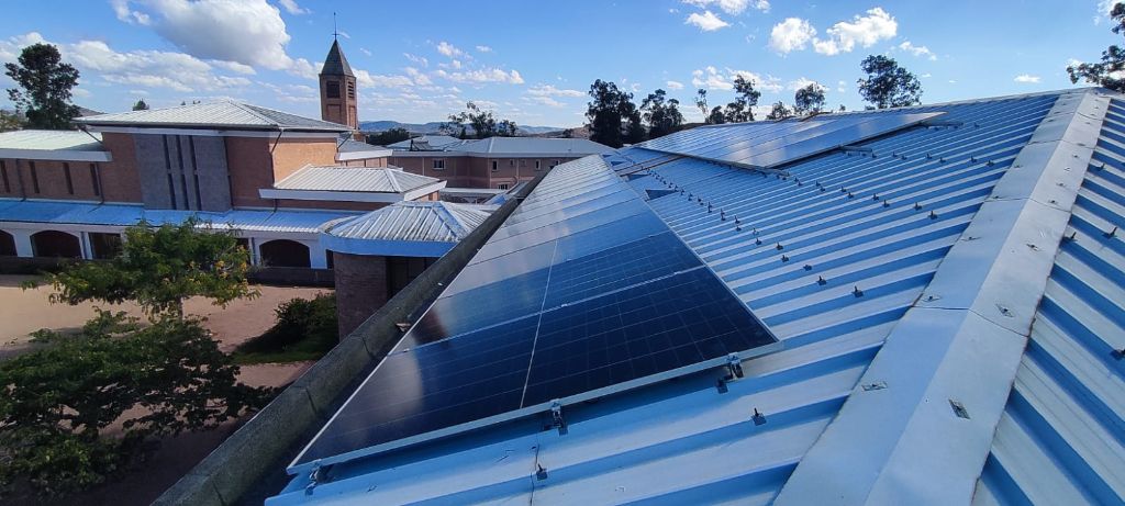Panneaux solaires sur toiture métallique bleue du couvent de Fianarantsoa — clocher en arrière-plan