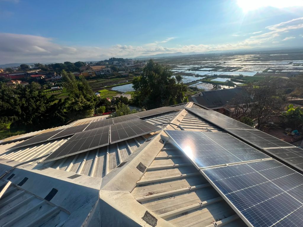 Panneaux solaires en toiture avec vue panoramique sur rizières inondées et village malgache