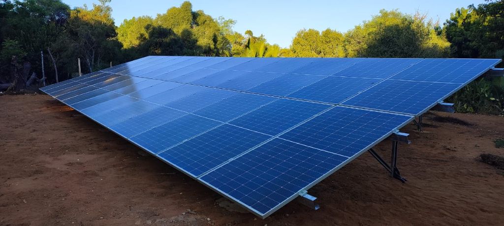 Champ de panneaux solaires sur structure métallique au sol — terre rouge caractéristique de Madagascar, végétation tropicale