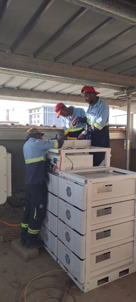 Techniciens Alona en uniformes bleus raccordant des racks de batteries SigEnergy